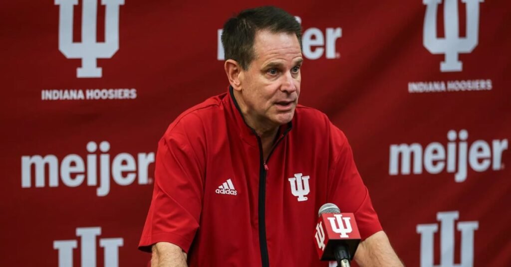 “Curt Cignetti speaking at an Indiana Hoosiers press conference in front of a red IU backdrop.”